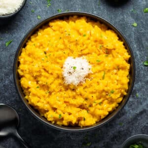 Risotto allo zafferano in a black bowl with parmesan cheese and chopped parsley.