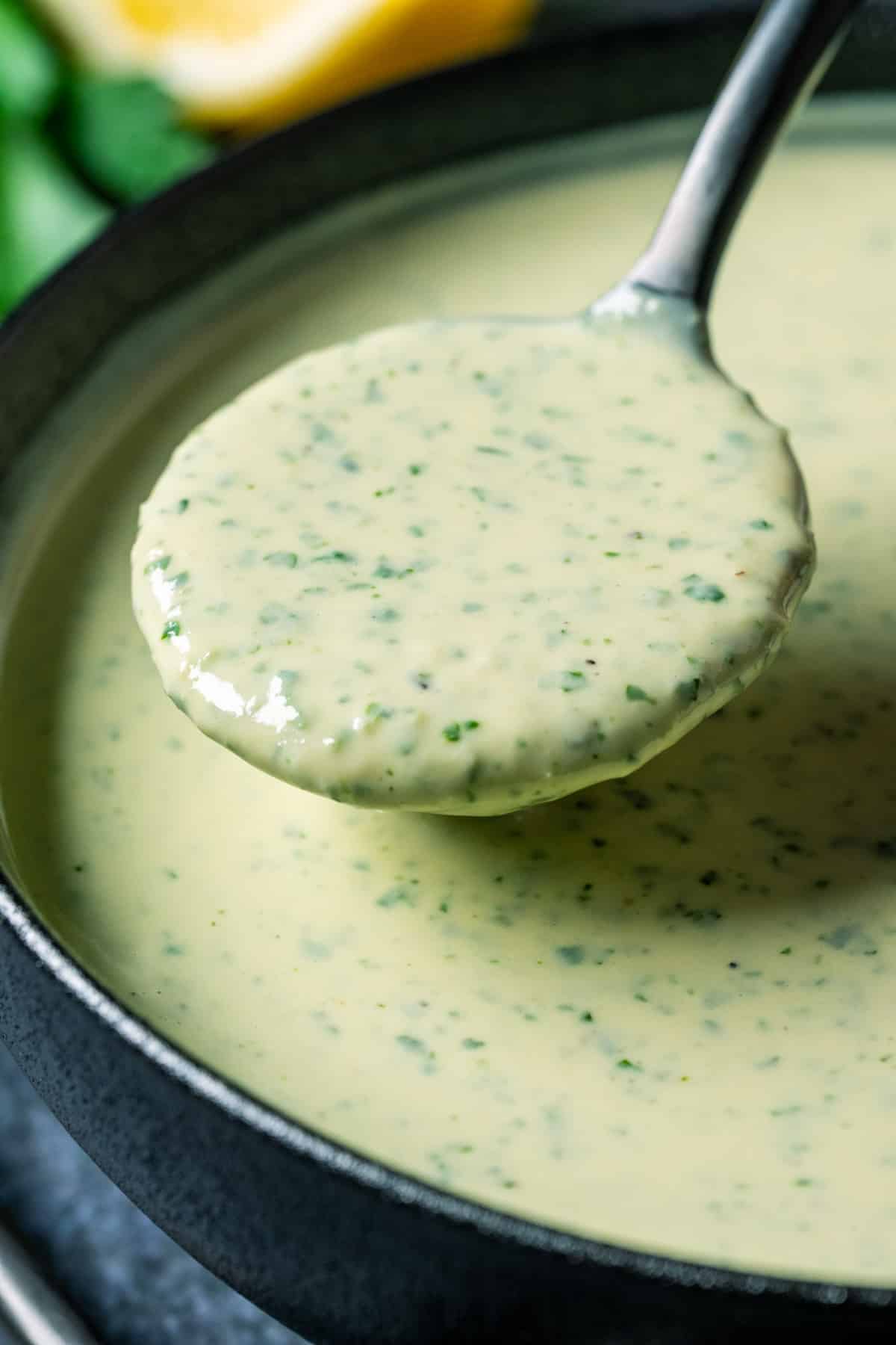 Lemon herb tahini in a black bowl with a spoon.