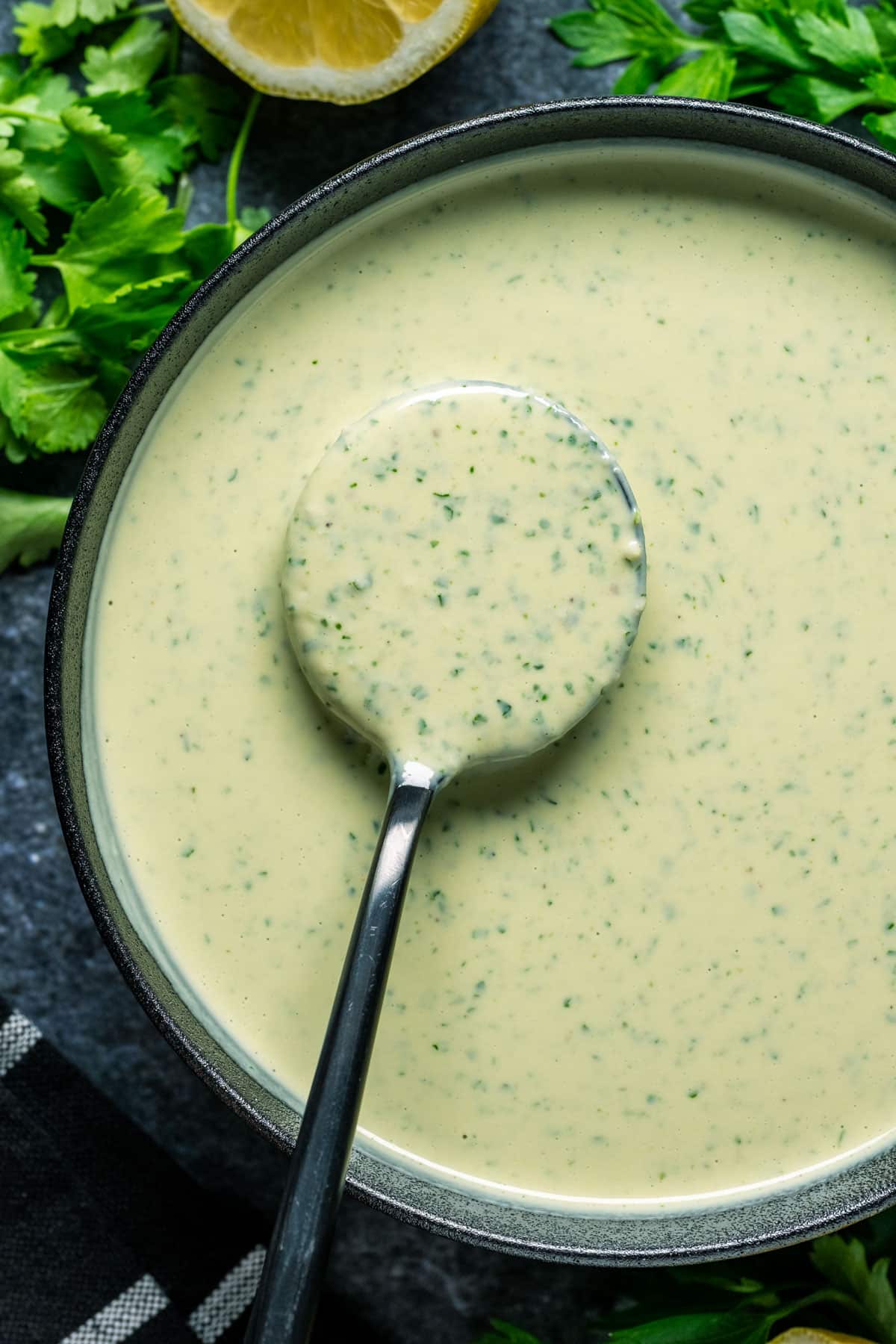 Tahini herb sauce in a black bowl with a spoon.