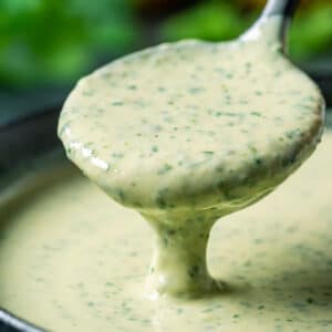 Lemon herb tahini sauce in a black bowl with a spoon.
