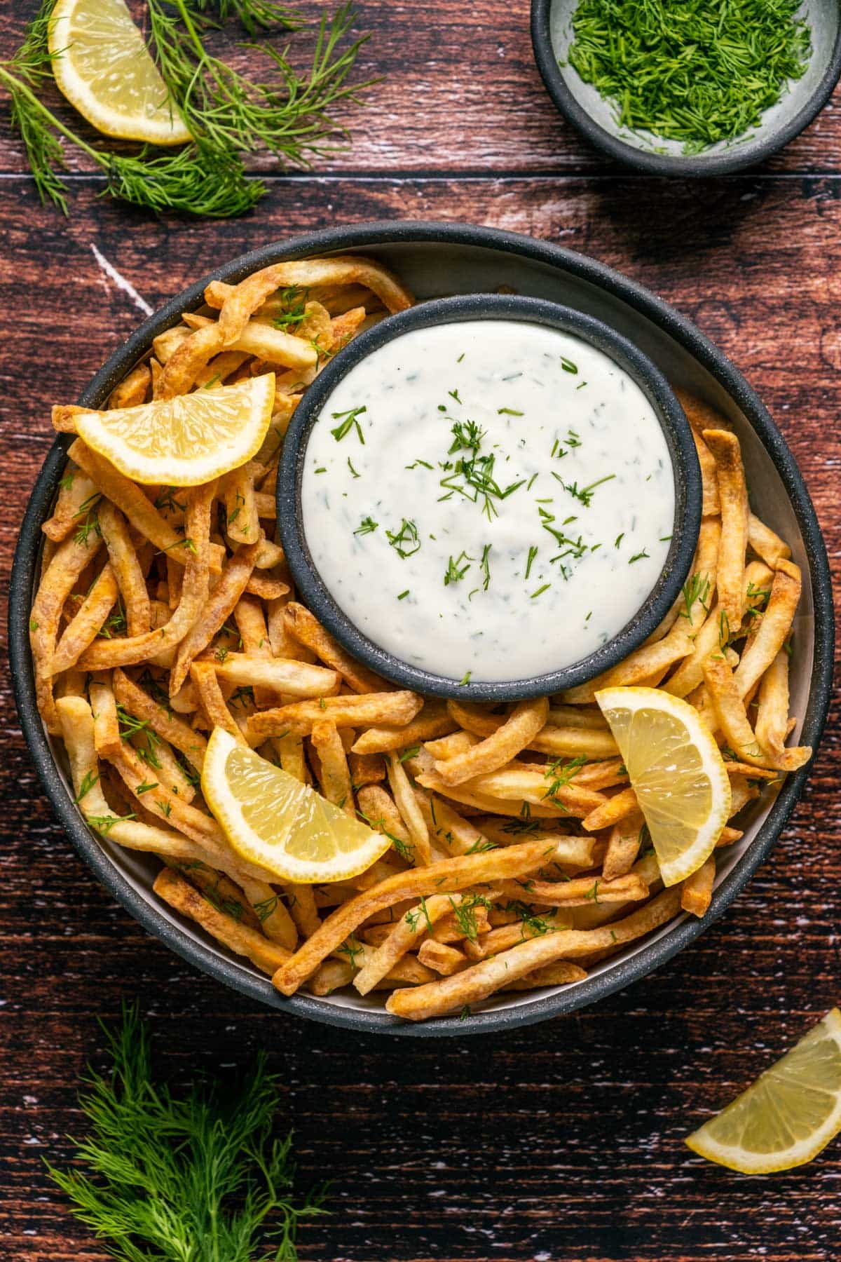 Lemon dill aioli topped with a sprinkle of dill on a plate with chips and lemon slices.