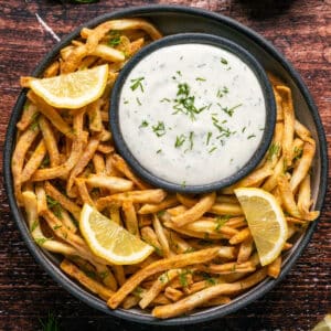 Lemon dill aioli topped with a sprinkle of dill on a plate with chips and lemon slices.