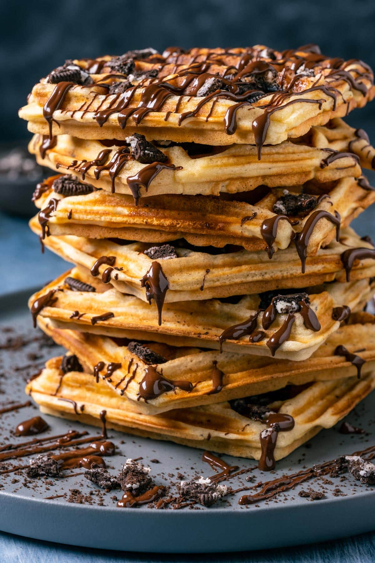 Stacked Oreo Waffles drizzled with melted chocolate on a gray plate.